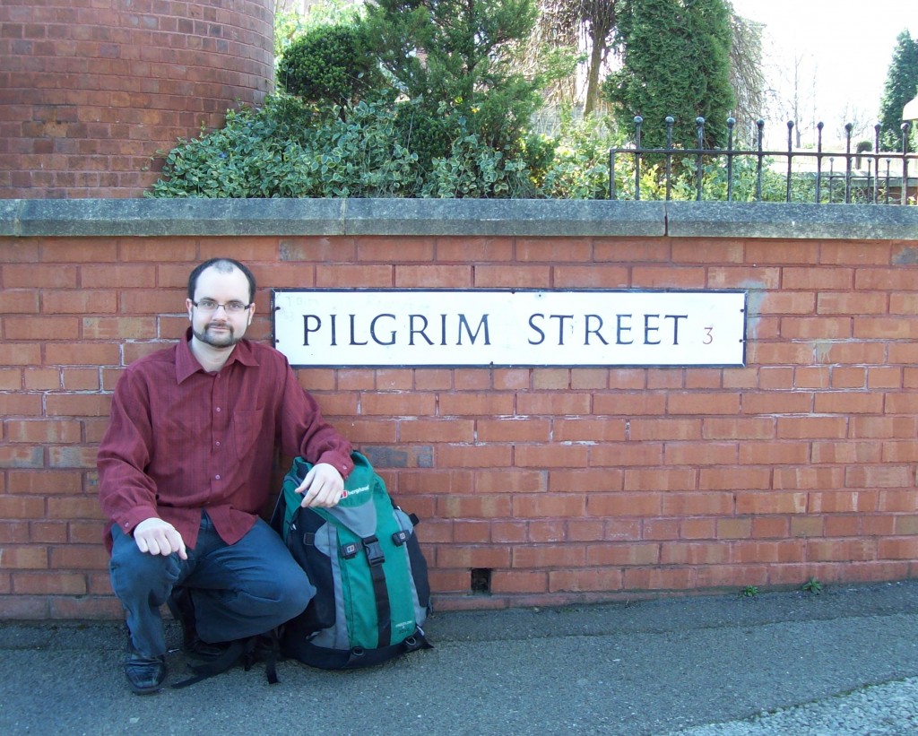Symon Hill crouched by a sign for Pilgrim Street
