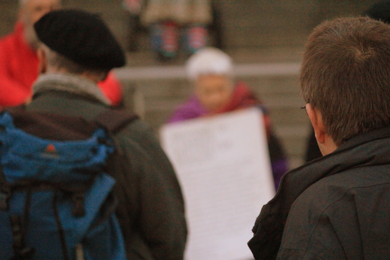 Quaker worship with two people with their backs to the viewer and out of focus a woman holding a sign about Quakers.